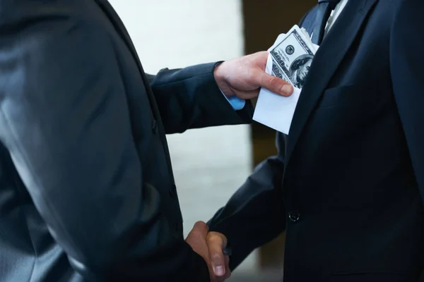 The rotten egg in the corporate world - deceptive deals. Two corporate businessmen shaking hands while one man places money in the otherampamp039s pocket. — Stock Photo, Image