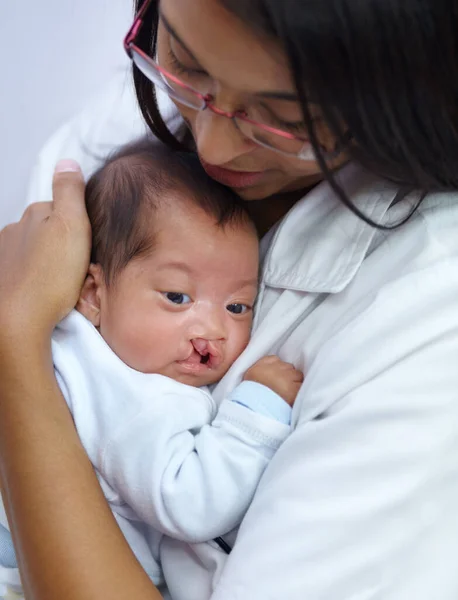 Donner du réconfort est la clé de sa profession. Prise de vue d'une jeune infirmière tenant un bébé ayant une fente palatine. — Photo