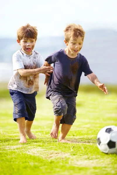 Mám přátelskou hru. Dva roztomilí malí kluci hrát fotbal spolu venku, zatímco pokrytý bahnem. — Stock fotografie