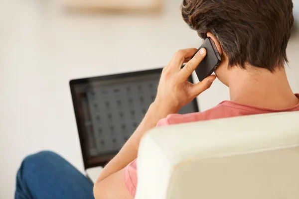 Profiteren van het gemak dat draadloze technologie biedt. Achteraanzicht van een jongeman aan het praten op zijn mobiel terwijl hij zijn laptop gebruikt. — Stockfoto