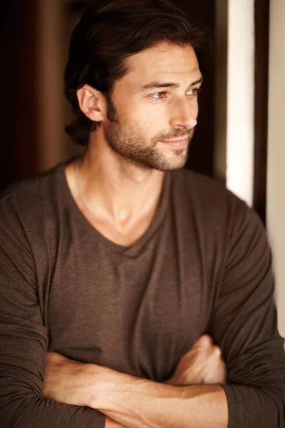 Content with his lot in life. A handsome young man gazing out of a window with his arms folded. — Stock Photo, Image