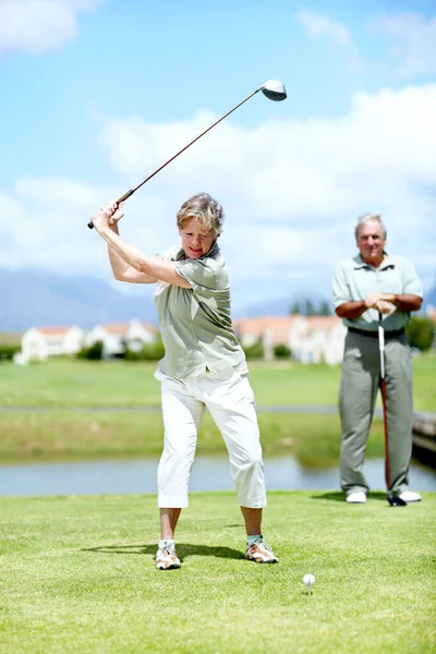 She has perfected her swing over the years. Image of a mature woman in full swing during a game of golf with her husband. — Stock Photo, Image