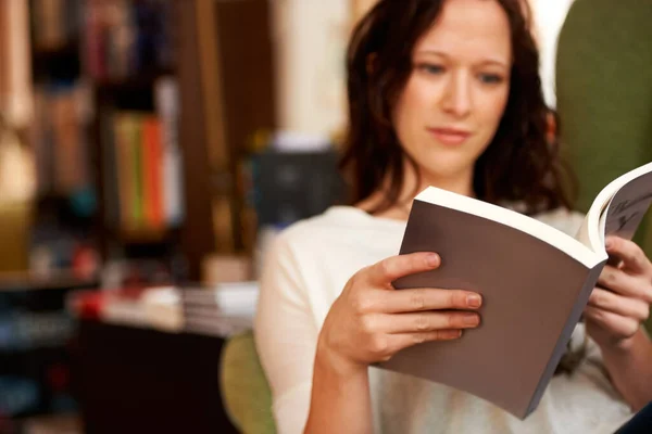 Ondergedompeld in woorden. Een jonge vrouw die rustig een boek leest terwijl ze in een stoel zit. — Stockfoto