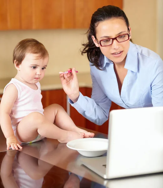 An extra hand would be useful. Shot of a single mom feeding her baby while trying to work on her laptop. — Stock Photo, Image