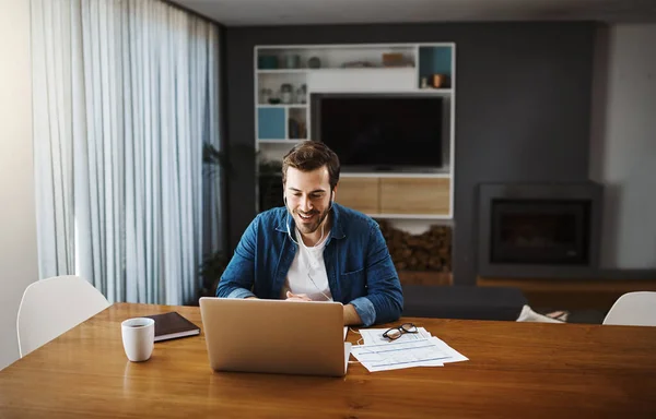 Seu negócio ainda como de costume, mesmo em casa. Tiro de um belo jovem empresário sentado e usando seu laptop para atender uma chamada de vídeo enquanto trabalhava em casa. — Fotografia de Stock