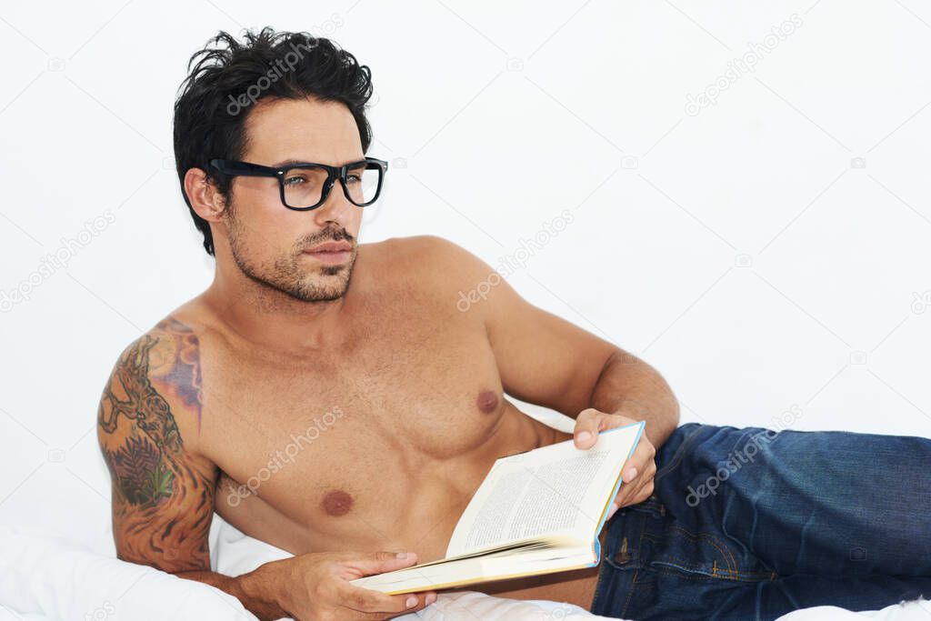 Enjoying a deep read.... Shot of a handsome young man lying on his bed reading a book.