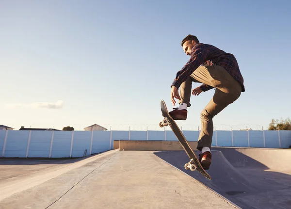 Un día genial en el parque de patinaje. Un joven haciendo trucos en su monopatín en el parque de skate. — Foto de Stock