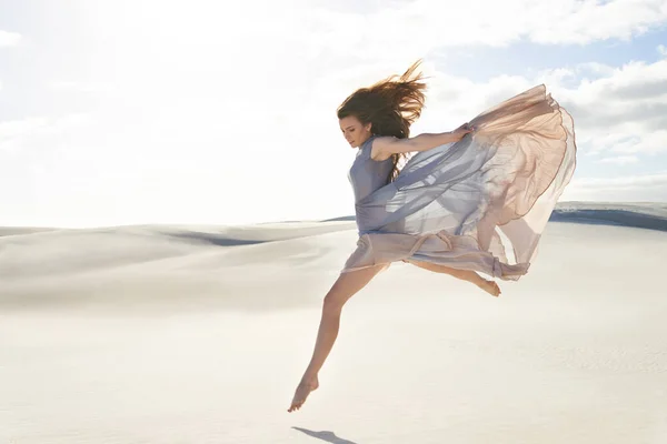 Svoboda a izolace na pláži. Boční pohled na krásnou mladou ženu v tekoucích šatech skákání přes písek. — Stock fotografie