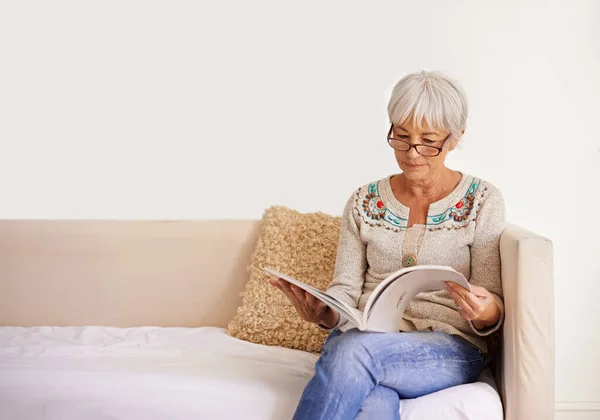 A entrar numa leitura pacífica. Tiro de uma mulher sênior lendo um livro enquanto sentado em um sofá. — Fotografia de Stock