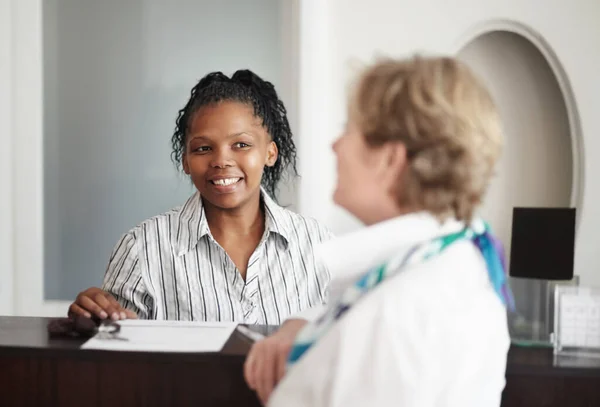 Omsorgsfull och vänlig hjälp. En receptionist som ger en äldre kvinna nycklarna till sitt hotellrum.. — Stockfoto