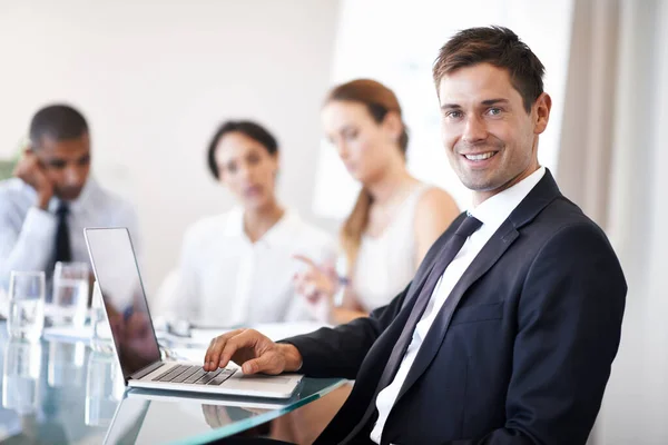 Siempre está conectado y disponible. Retrato de un hombre de negocios feliz usando un portátil durante una reunión. —  Fotos de Stock