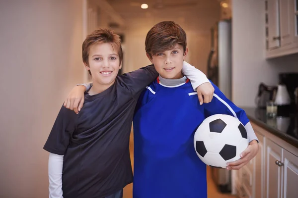 Pojkar kommer att vara pojkar. Porträtt av två unga pojkar i sportkläder står inomhus med en fotboll. — Stockfoto