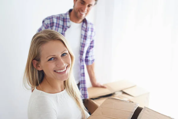 Heureuse d'avoir sa propre maison. Une femme souriante portant une boîte en carton marron pendant que son petit ami regarde. — Photo