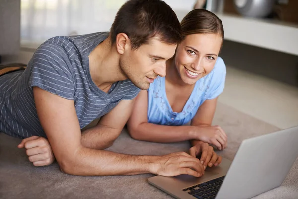 Få all deras information online. Skjuten av ett lyckligt ungt par med en bärbar dator på golvet tillsammans. — Stockfoto