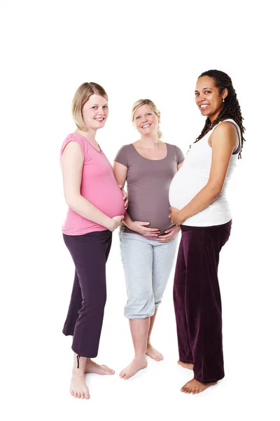 Je me sens déjà protecteur. Trois femmes enceintes souriant largement à la caméra debout sur un fond blanc tenant leurs estomacs. — Photo