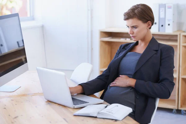 Moderní ženy to všechno zvládnou. Těhotná podnikatelka pracující na notebooku ve své kanceláři. — Stock fotografie