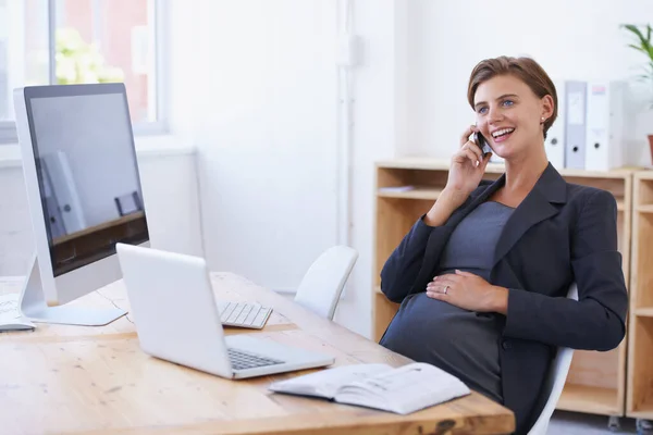 Beru si přátelskou radu pro dítě. Těhotná podnikatelka, která má příjemnou konverzaci na telefonu u svého stolu v kanceláři. — Stock fotografie