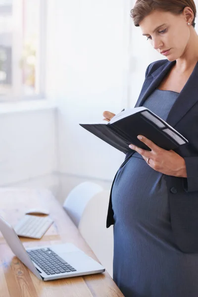 Potvrzuji její mateřskou dovolenou. Těhotná podnikatelka čtení její denní plánovač ve své kanceláři. — Stock fotografie