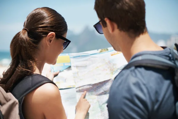 Trazando la mejor ruta a la playa. Fotografía de una joven pareja mirando un mapa mientras está de pie en una playa. — Foto de Stock