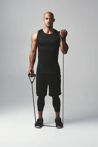 La resistencia te llevará a todas partes. Retrato de estudio de un joven atlético haciendo ejercicio con una banda de resistencia sobre un fondo gris. — Foto de Stock