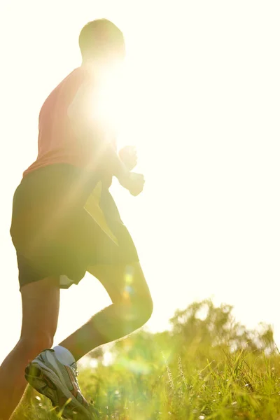 Rennend in het zonlicht. Achteraanzicht van een jongeman die buiten rent op een bergpad. — Stockfoto