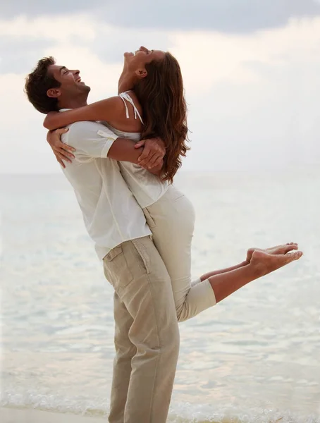 Een avond omhelzing - romantiek. Jongeman tillen zijn prachtige vriendin in de lucht, terwijl op het strand. — Stockfoto