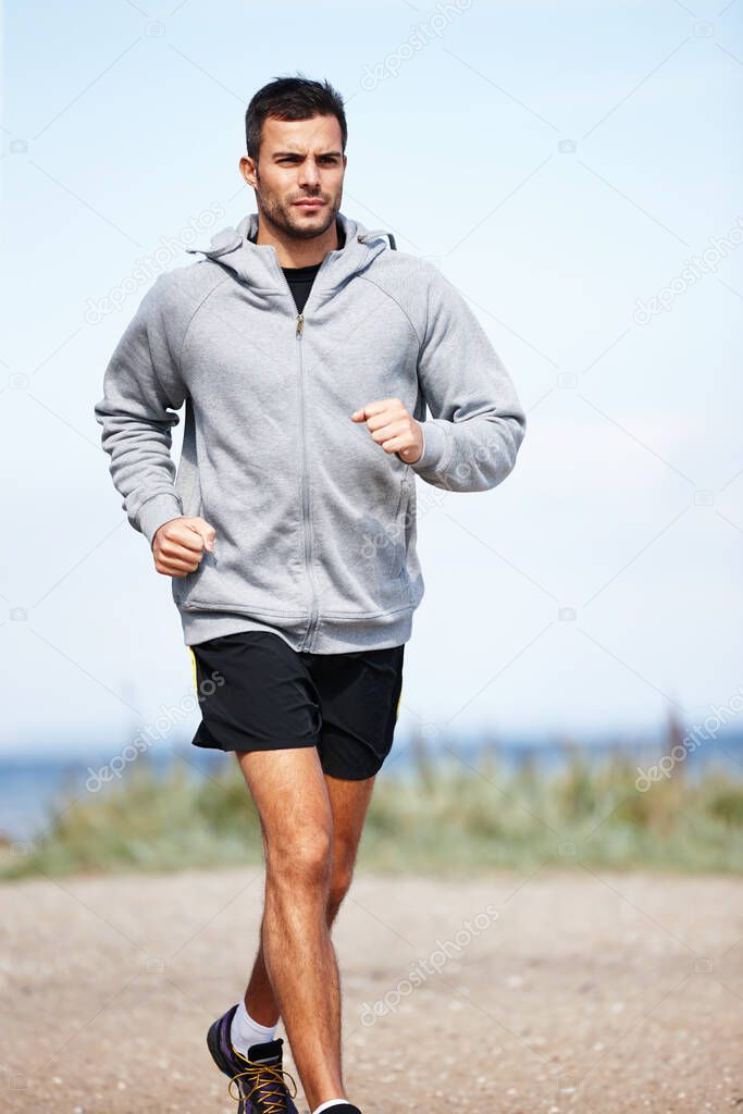 Taking a morning jog on the beach. Shot of a handsome young man running on the beach.