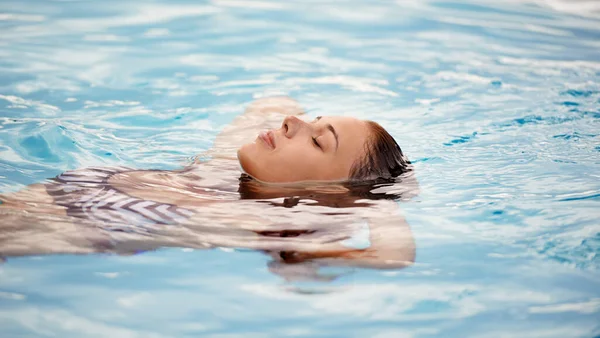 Como flotar en una nube. Recortado disparo de una hermosa mujer joven relajándose en una piscina. — Foto de Stock