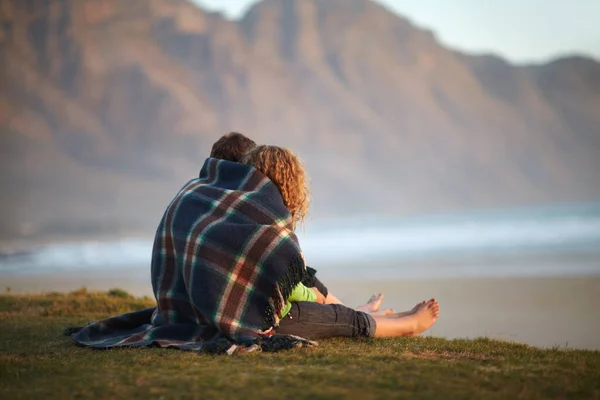 A apreciar a vista. Bonito casal jovem envolto em um cobertor enquanto sentado em uma margem do rio. — Fotografia de Stock
