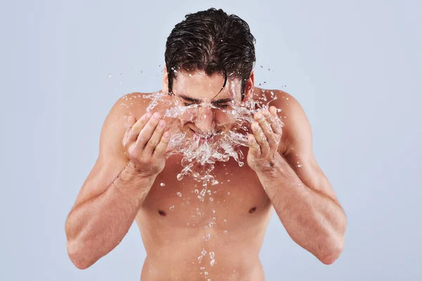 Rein erfrischend. Studioaufnahme eines barbusigen jungen Mannes, der sich Wasser ins Gesicht spritzt. — Stockfoto