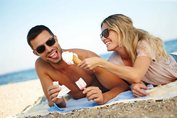 おいしいことになるわ。幸せな若いカップルのショット晴れたビーチに横たわっている間にアイスクリームを食べる. — ストック写真