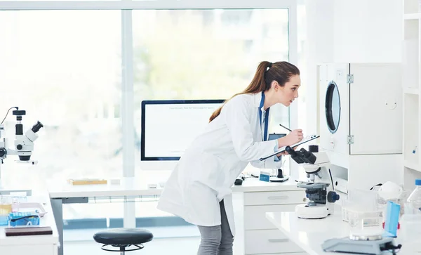 Παρατηρώντας και κρατώντας σημειώσεις. Καλλιεργημένη λήψη μιας στοχευμένης νεαρής γυναίκας επιστήμονα που διεξάγει πειράματα μέσα σε ένα εργαστήριο κατά τη διάρκεια της ημέρας. — Φωτογραφία Αρχείου