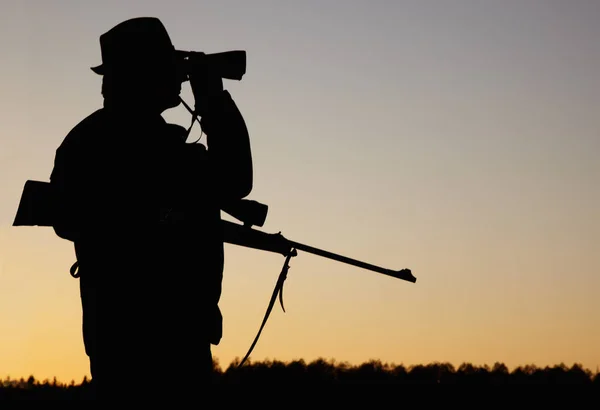 Wildtiere aufspüren. Die Silhouette eines Wildhüters, der sein Gewehr in der Hand hält und durch sein Fernglas auf den Sonnenaufgang im Freien blickt. — Stockfoto