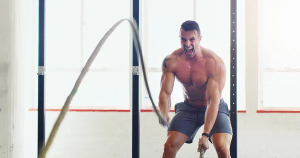 No necesitas una máquina para serlo. Tiro de un joven haciendo ejercicio con cuerdas de batalla en un gimnasio. — Foto de Stock