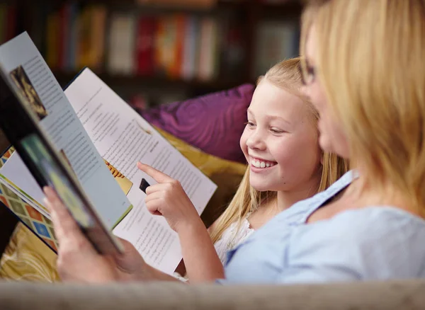 A ler juntos. Uma menina bonita sentada ao lado de sua mãe enquanto eles lêem um livro. — Fotografia de Stock