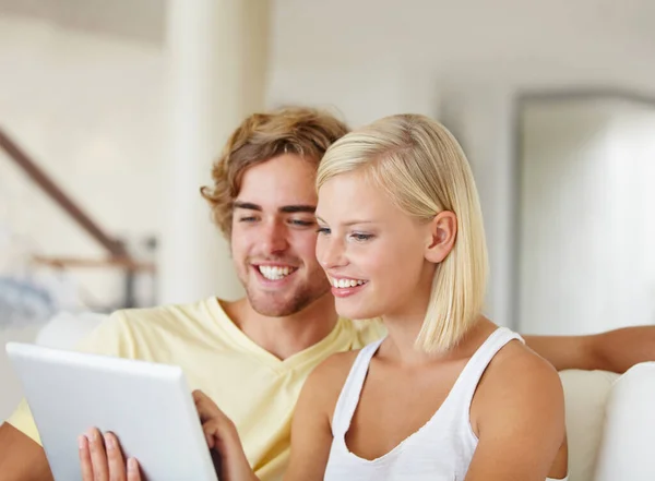 Video chat con la famiglia. Una giovane coppia felice utilizzando un tablet insieme nel loro salotto. — Foto Stock