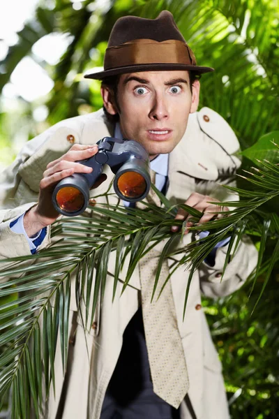 Ich kann das nicht glauben. Schockierter Privatdetektiv spioniert mit Fernglas jemanden aus dem Gebüsch aus. — Stockfoto