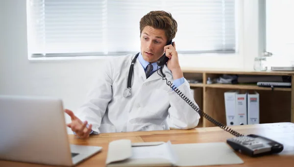 Discuter du statut d'un patient. Tourné d'un jeune médecin assis dans son bureau et parlant au téléphone. — Photo