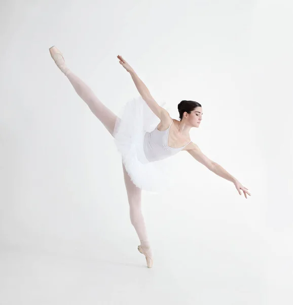 Баланс имеет решающее значение. Элегантный молодой балерина танцует на пуантах на белом фоне в положении penche. — стоковое фото