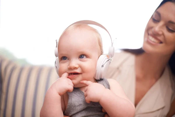 What you listening to. Shot of an adorable baby girl wearing headphones while sitting with her mother. — Stock Photo, Image