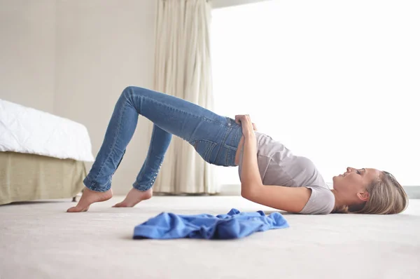 Theyre just too small. A young woman struggling to pull on her jeans. — Stock Photo, Image