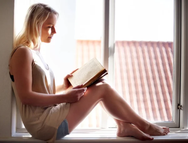 Inclusa nel suo romanzo. Una giovane donna che si rilassa su un davanzale e legge un romanzo coinvolgente. — Foto Stock