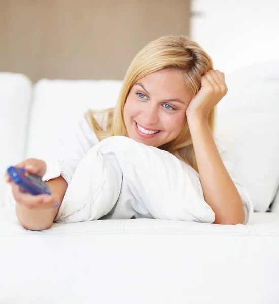 Filme im Bett. Eine attraktive junge Frau wechselt mit der Fernbedienung die Kanäle. — Stockfoto