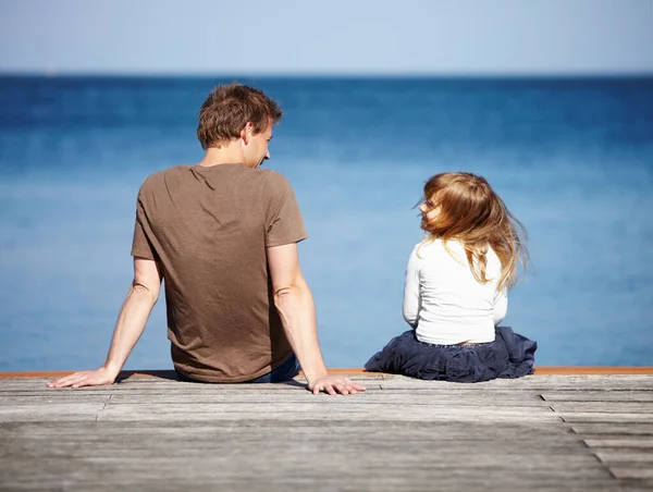 和爸爸分享她的梦想一个年轻的父亲和他的女儿坐在一个以大海为背景的码头上的后视镜. — 图库照片