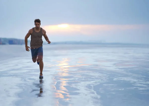 Inspirációt találni a fitnessz segítségével. Egy jóképű fiatalember edz a parton kora reggel.. — Stock Fotó