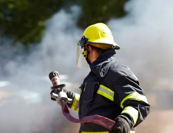 Han har läget under kontroll. En kaukasisk brandman som håller i en slang och omges av röken från brandhärden har precis släckts.. — Stockfoto