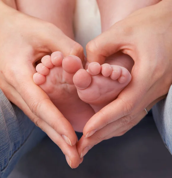 爱那些小东西。妈妈们双手合十的剪影，使她婴儿的脚周围有了一个心形. — 图库照片