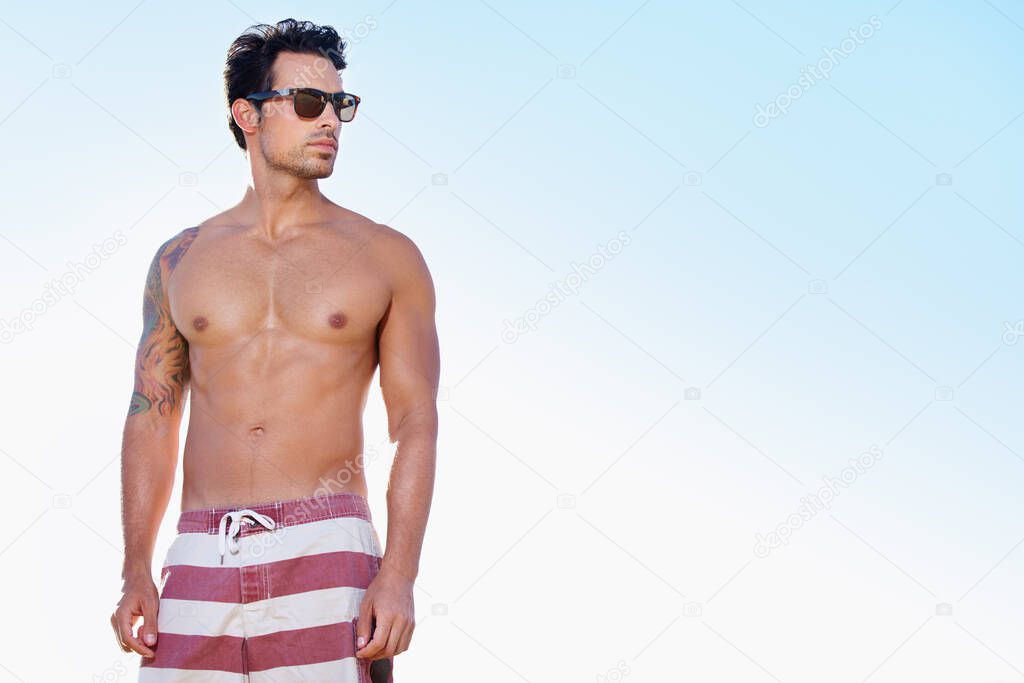 Beach cool. Waist up shot of a young man in swim trunks against a blue sky.