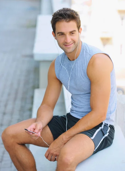 Bewegung stärkt ihn. Glückliche junge Joggerin sitzt draußen und hört Musik. — Stockfoto