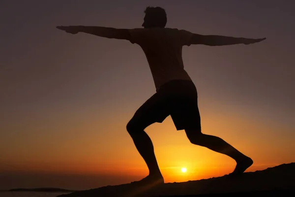 Estiramiento en la luz menguante. Silueta de un hombre haciendo ejercicios con la puesta de sol en el fondo. —  Fotos de Stock